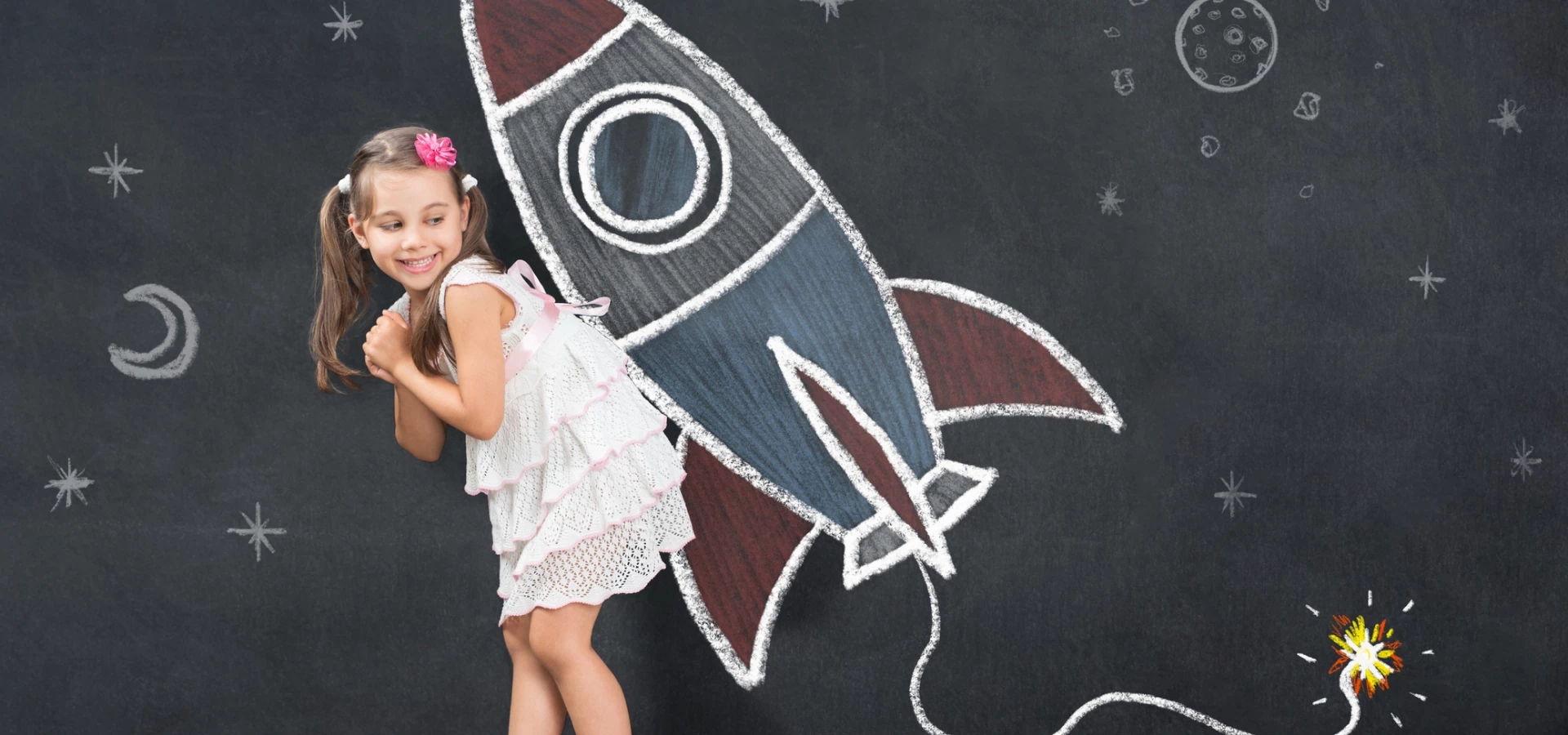 Dziewczynka stojąca przy rakiecie narysowanej na tablicy szkolnej